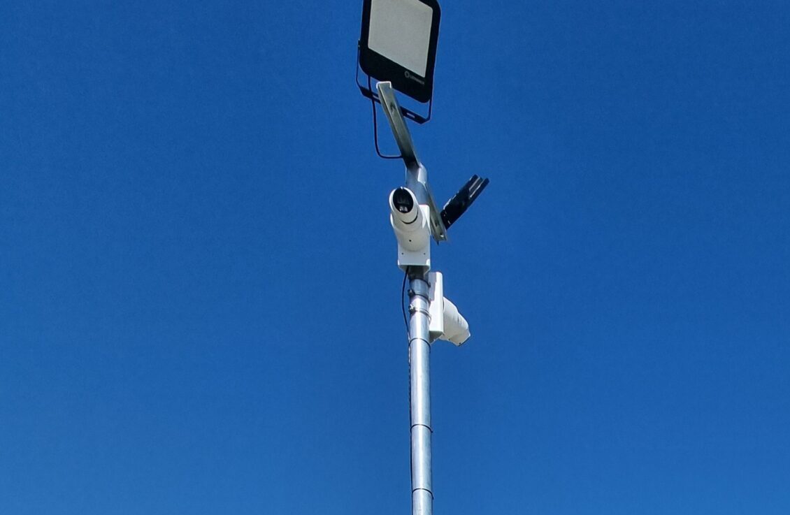 Security pole with CCTV cameras positioned along the main access road at a commercial storage yard to monitor vehicle movements.