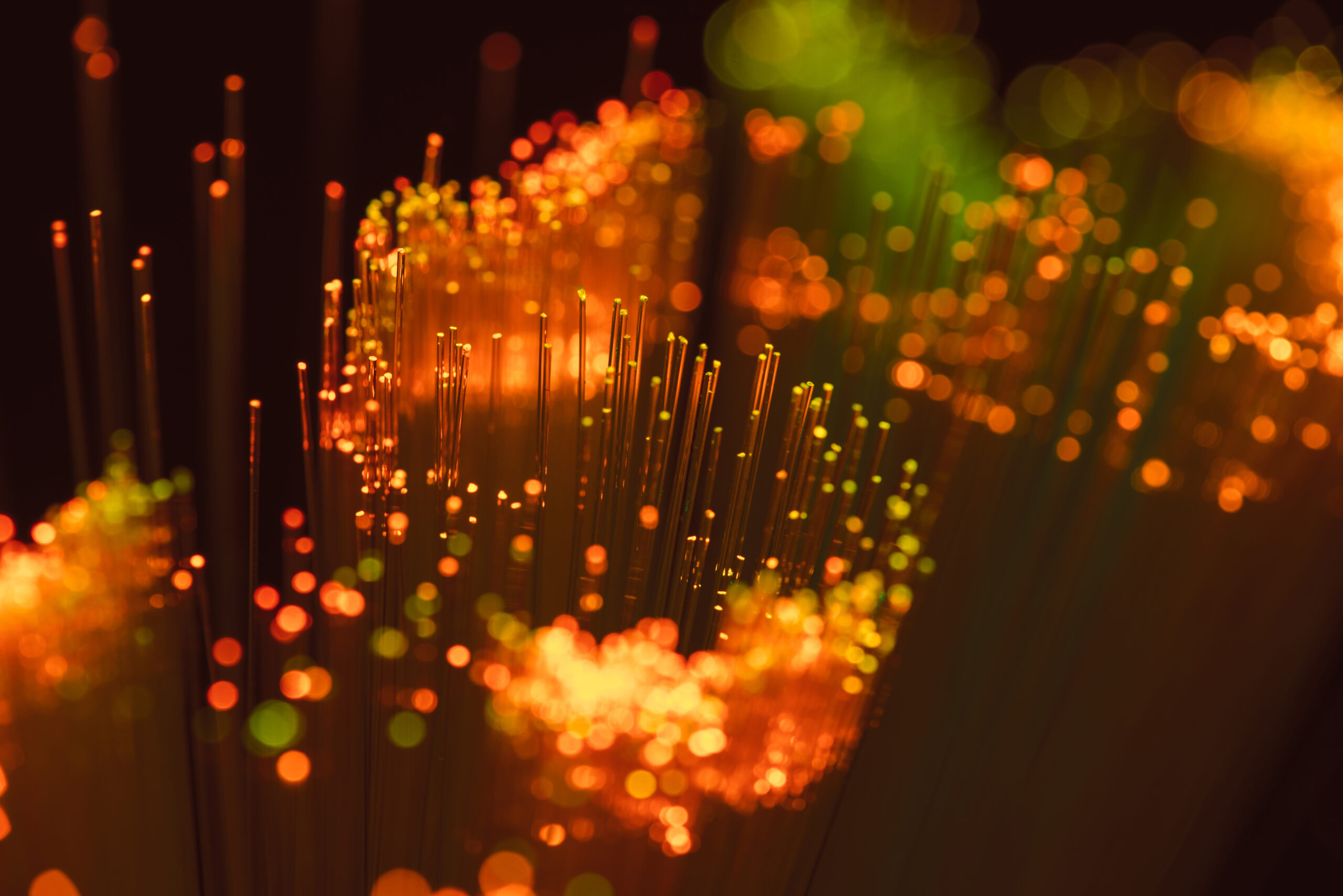 A macro view of illuminated fibre optic strands glowing with warm colours, representing high‑speed data transmission and modern fibre networking technology.