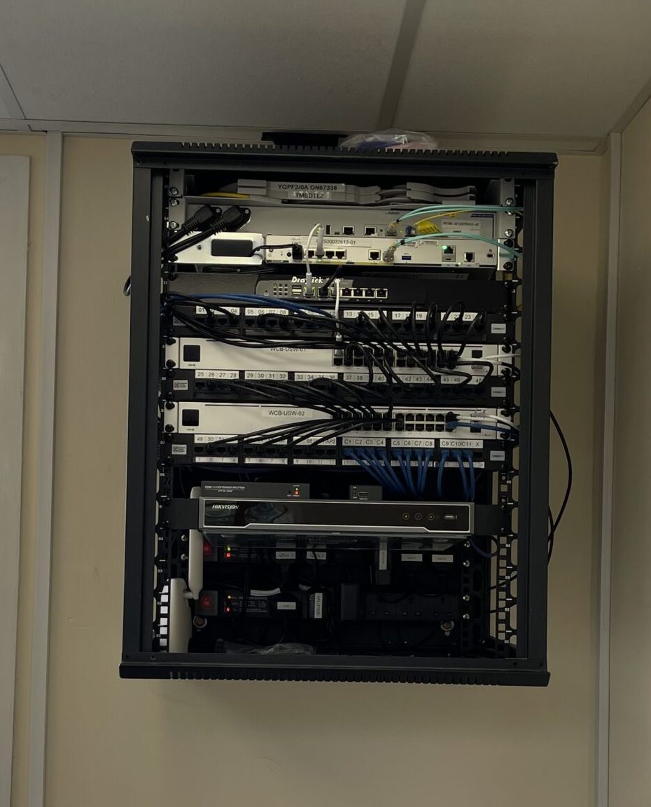 A wall-mounted data cabinet showing a network switch, fibre optic leads, and structured cabling for an internal network installation.