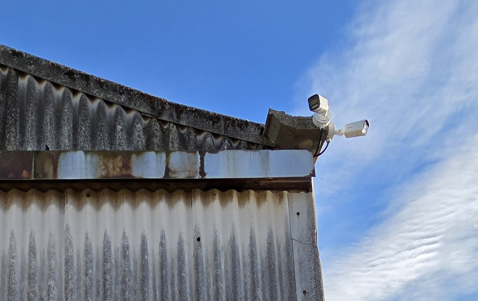 Two outdoor CCTV cameras installed on the edge of an industrial building roof to provide wide‑angle site surveillance.