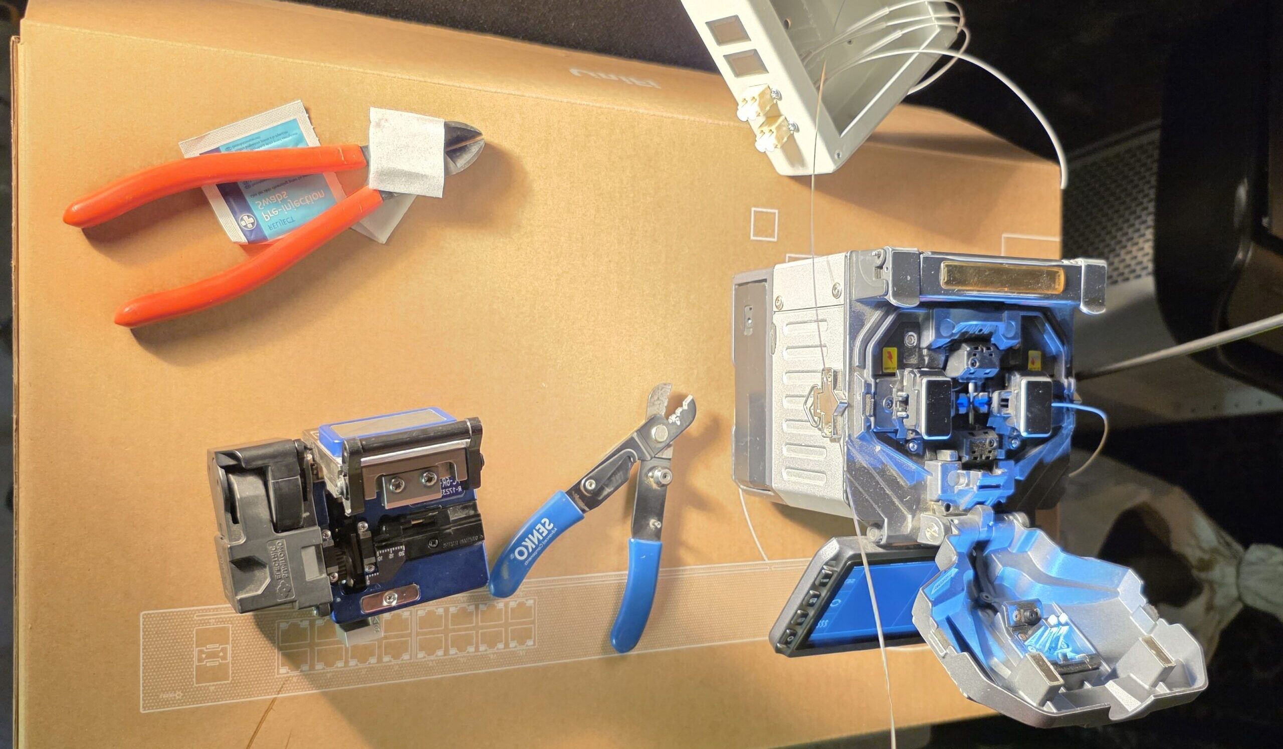 A workstation layout showing fibre optic splicing equipment, including a fusion splicer, cleaver, and fibre preparation tools.