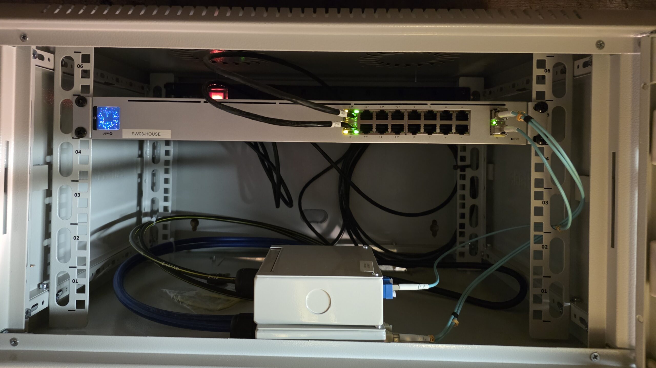 A wall-mounted data cabinet containing a network switch with active fibre and copper cabling as part of a structured cabling installation.