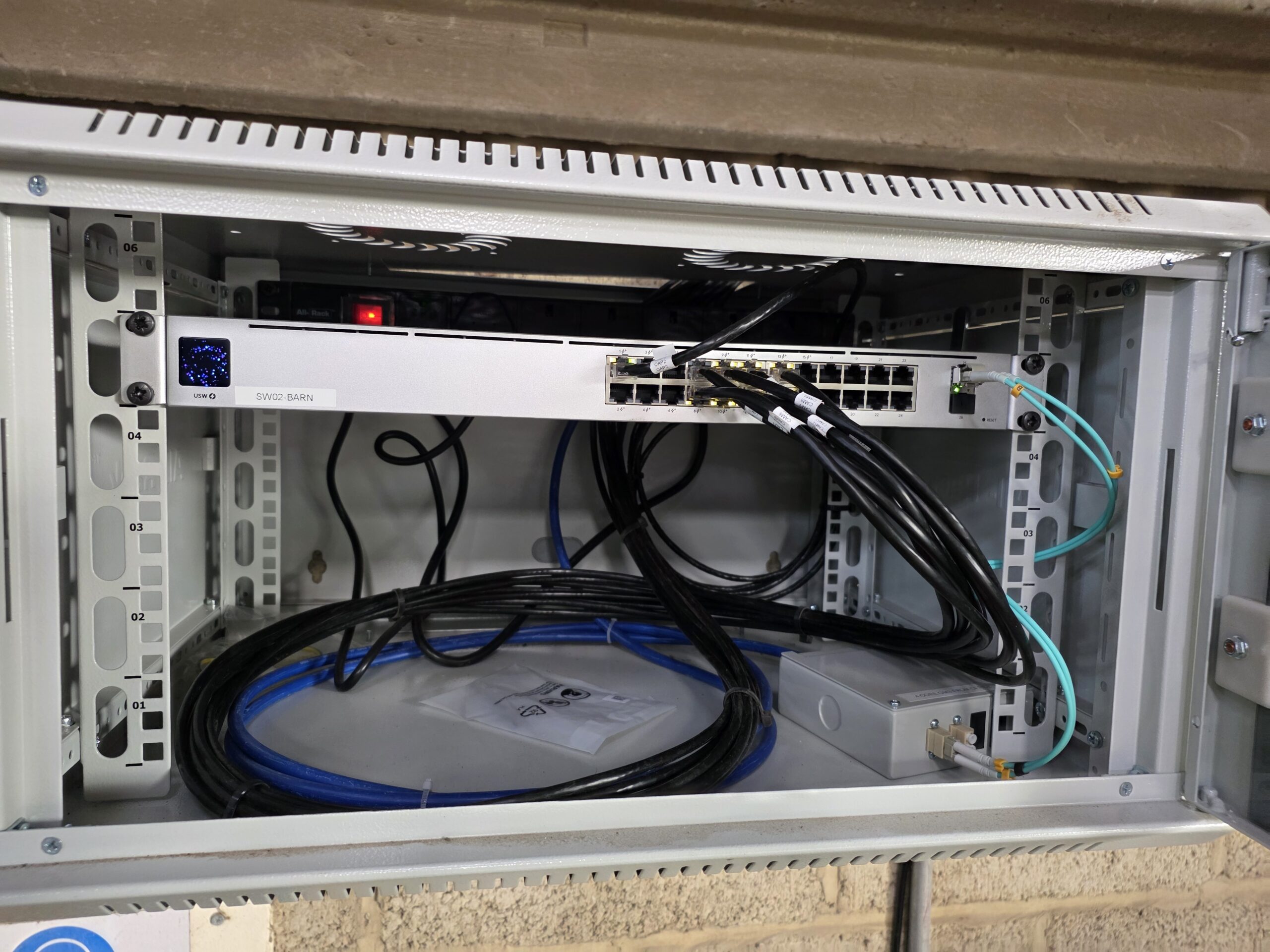 A wall-mounted data cabinet containing a network switch with organised copper and fibre cabling for a commercial network installation.