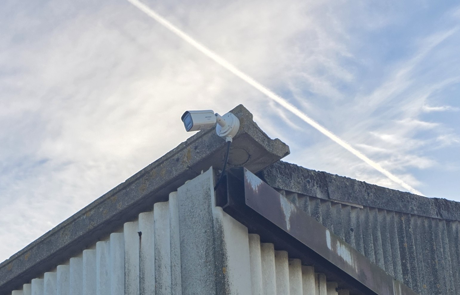 A weather-resistant CCTV camera fixed to the top edge of an industrial building for perimeter monitoring.