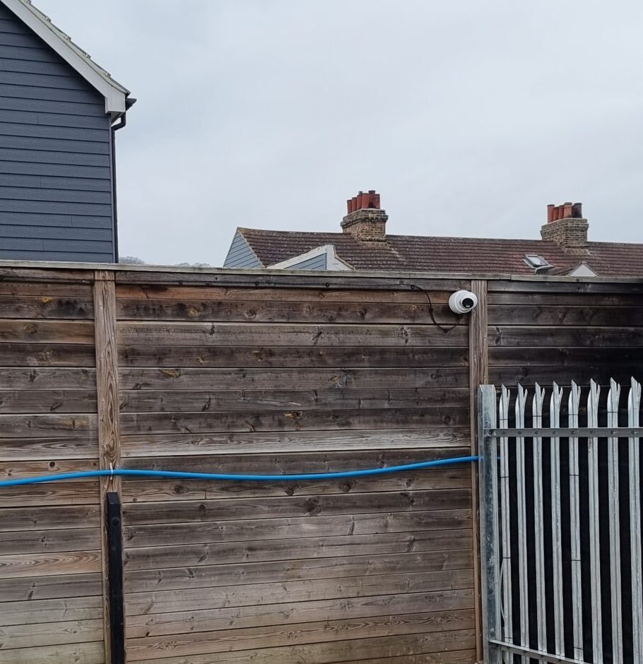 A CCTV camera mounted on a wooden fence to monitor the perimeter of a commercial yard and improve security coverage.