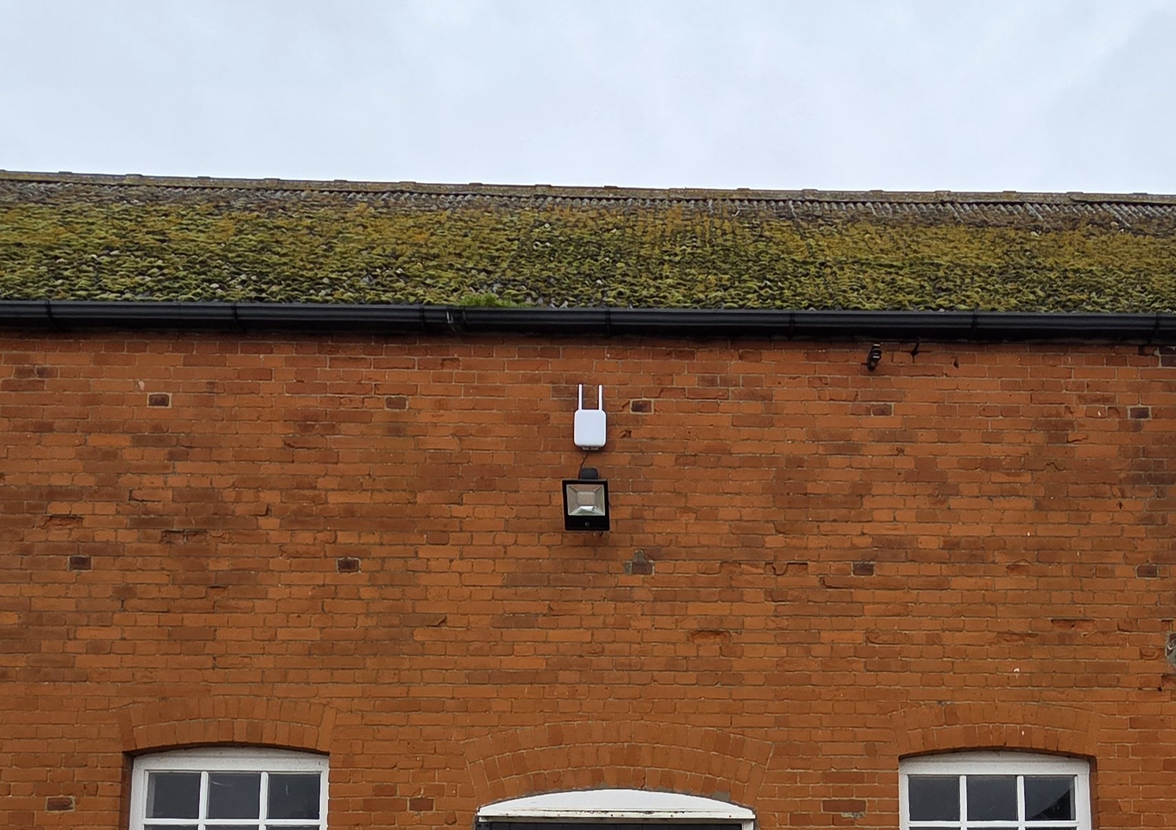 A wireless access point mounted on the exterior wall of a commercial building to extend outdoor Wi-Fi coverage.