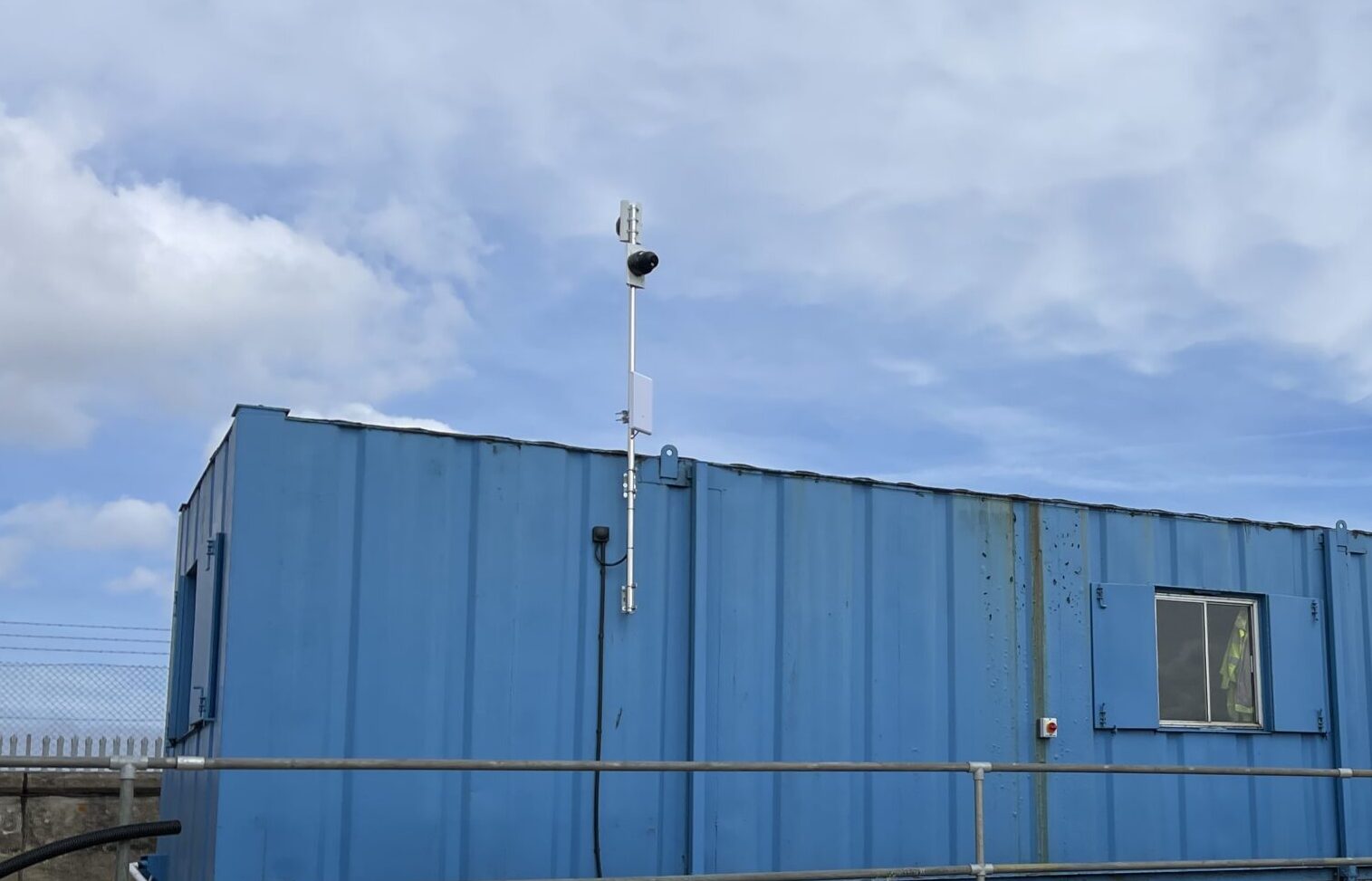 A CCTV camera mounted on a raised pole attached to a blue site cabin.
