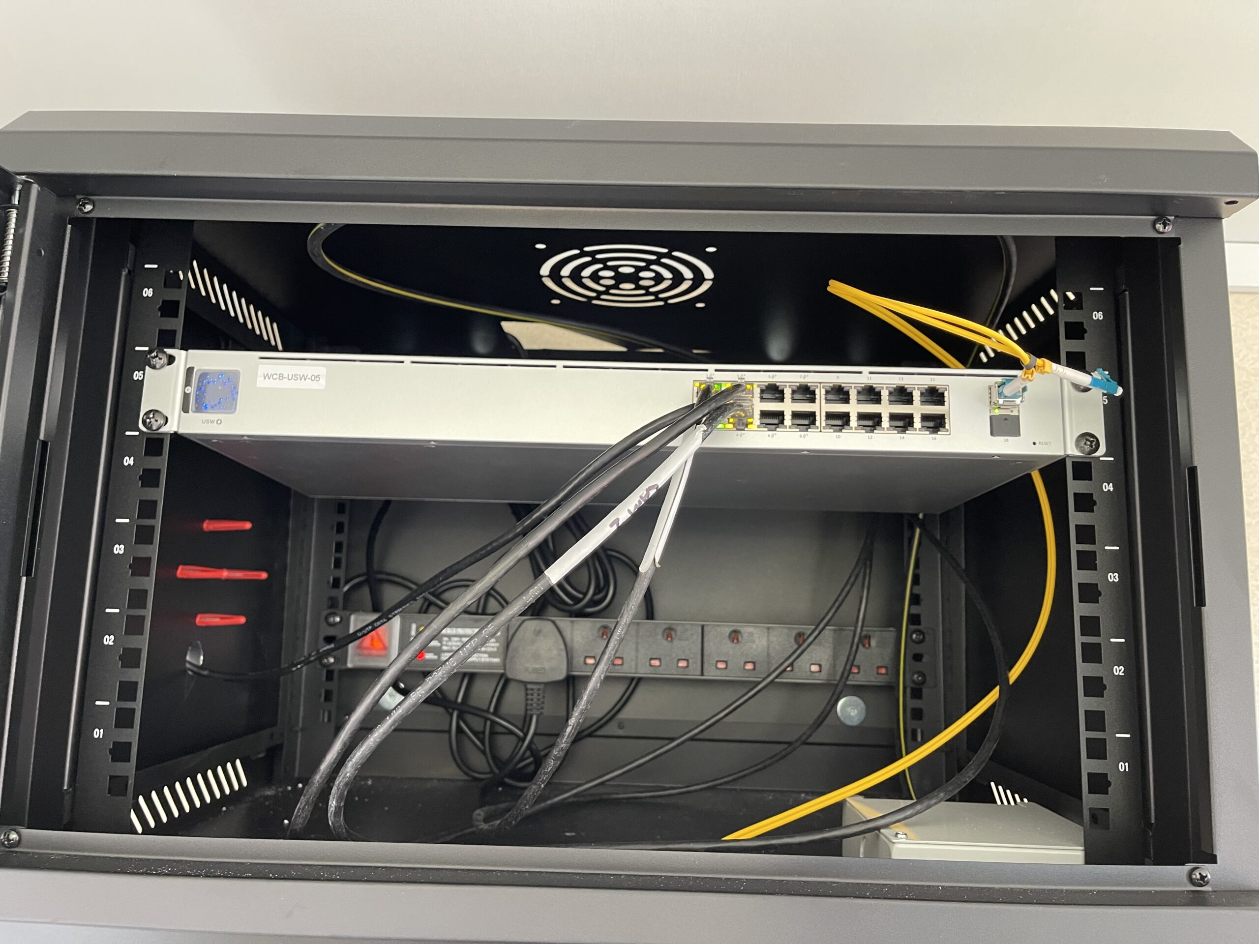 A wall‑mounted data cabinet containing network switches, patching, and power distribution as part of an office network installation.